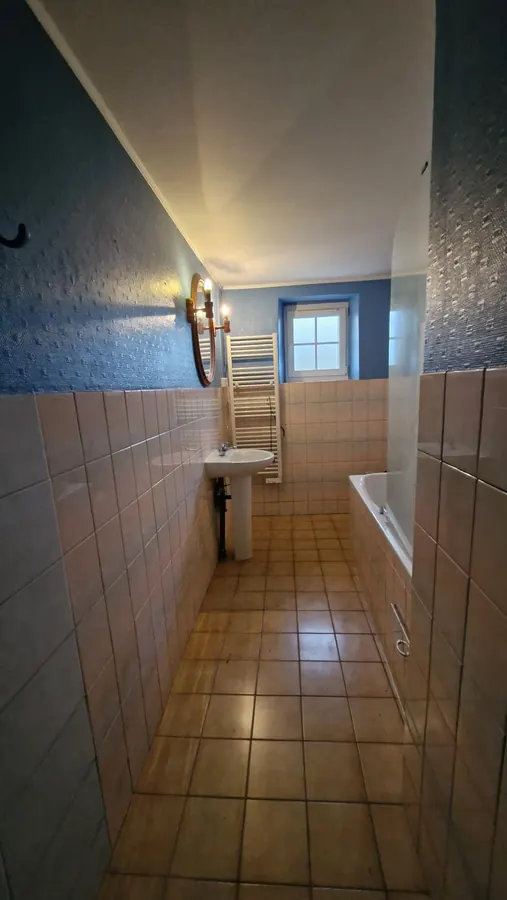 Pièce sanitaire carrelée avec baignoire et fenêtre en fond de pièce